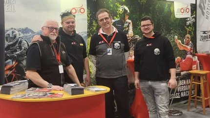 Vier Männer an einem Stand von Motorrad Hotels auf einer Messe