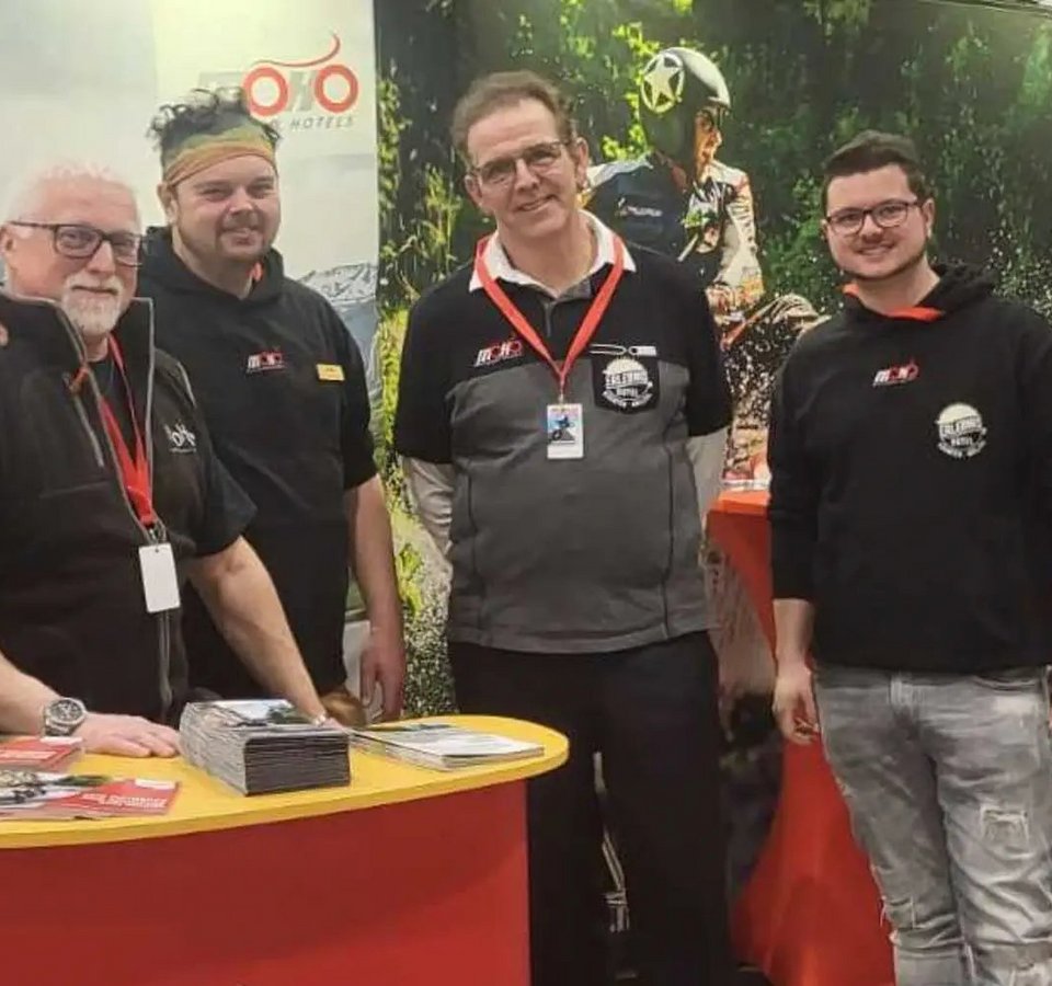 Vier Männer an einem Stand von Motorrad Hotels auf einer Messe