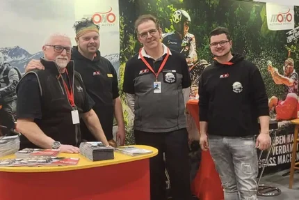 Vier mannen bij een Motorrad Hotels stand op een beurs