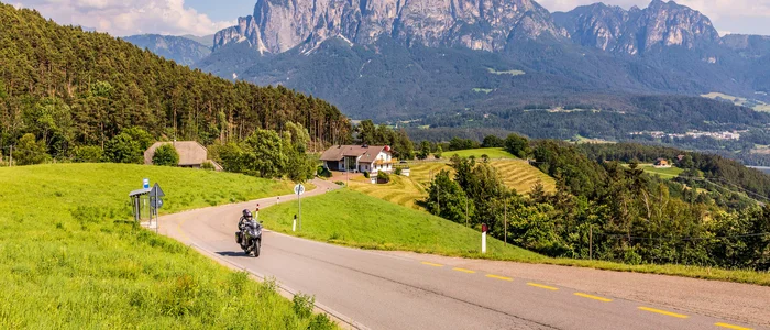 Motorcyclist riding on country road with alpine mountains in the background