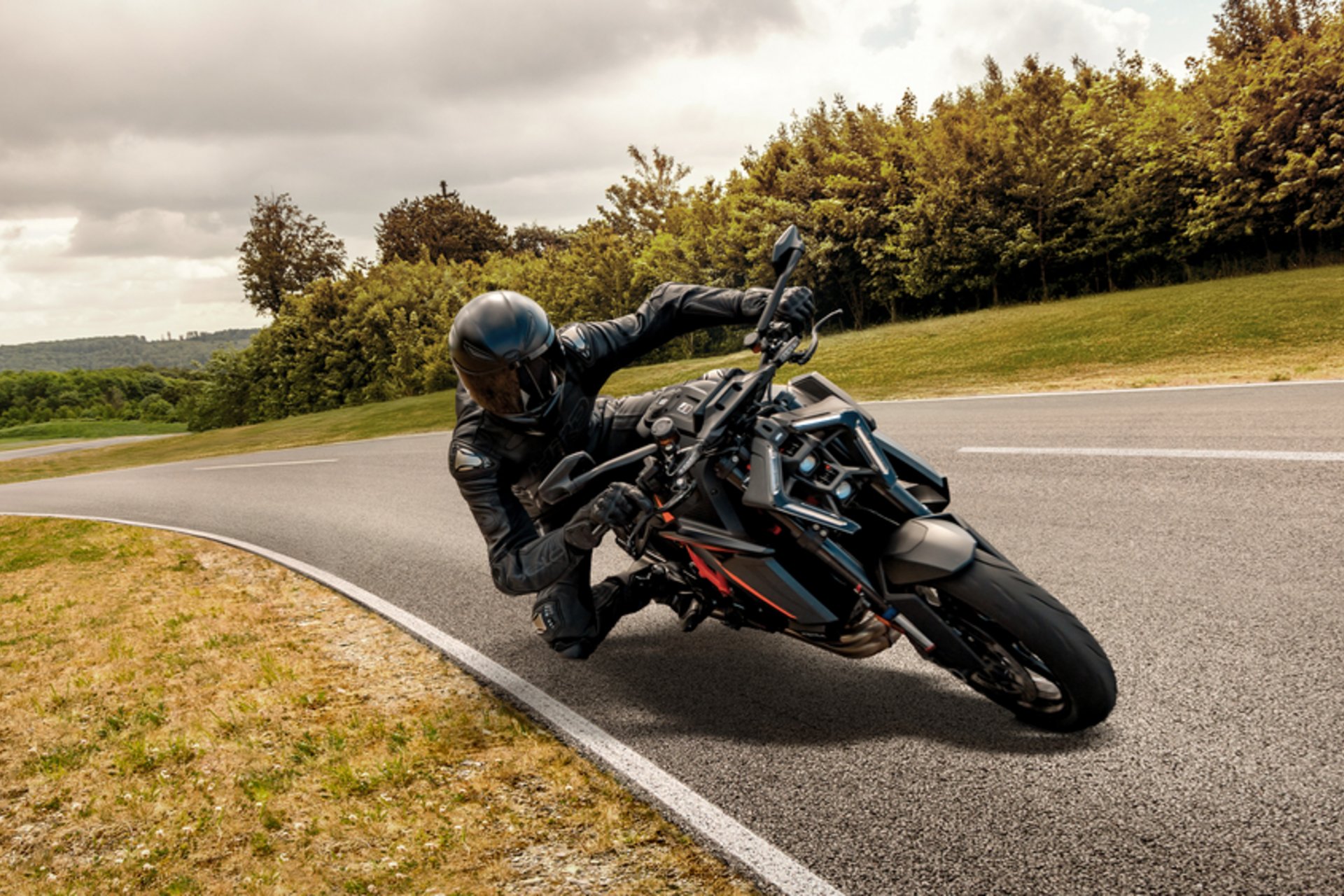 Motorcyclist in black gear leaning into a curve on a winding road