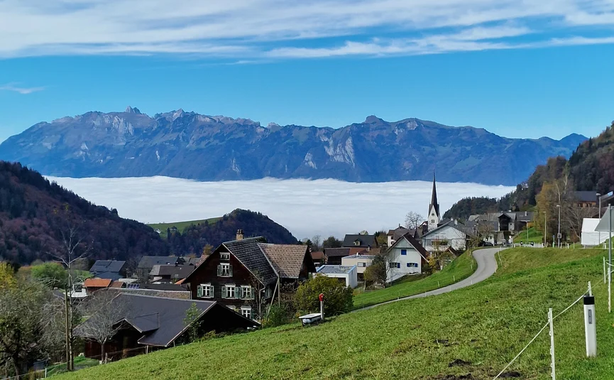 Village with green fields and mountains in the background under blue sky