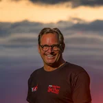 Mann in schwarzem T-Shirt lächelt vor Sonnenuntergang mit rotem Himmel