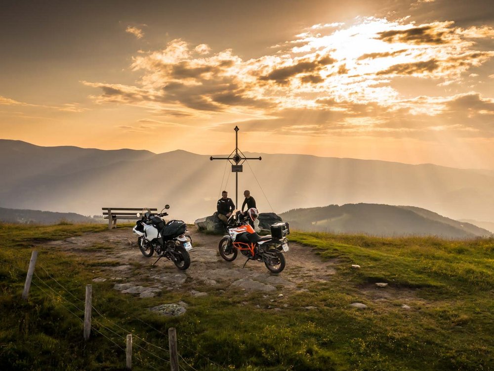 Dein Motorrad-Erlebnis © Moppetfoto.de Zwei Motorräder und zwei Personen bei einem Gipfelkreuz im Sonnenuntergang in den Bergen
