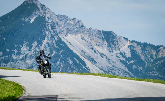Motorradfahrer auf Bergstraße vor großen Felsen und blauem Himmel