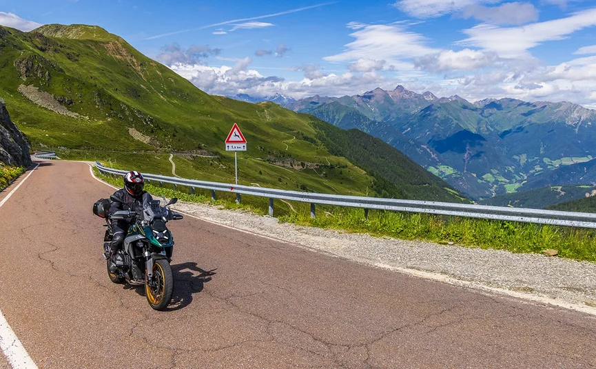 Stilfserjoch Motorradfahrer auf einer Bergstraße mit grünem Hügel und Bewölkung