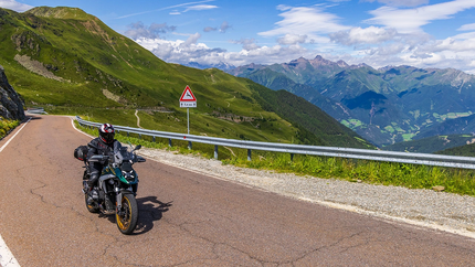 Motorcoureur rijdend op bergweg met groene heuvels en bewolking