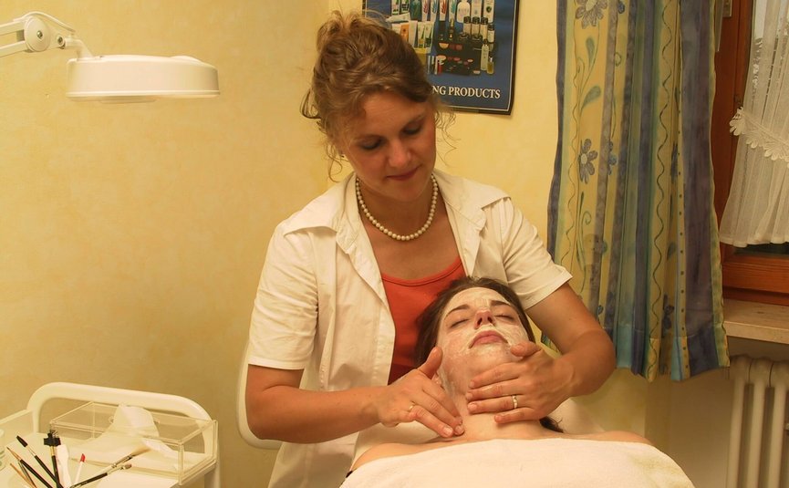 Kosmetikerin massiert Gesicht einer Frau mit Gesichtsmaske im Behandlungsraum