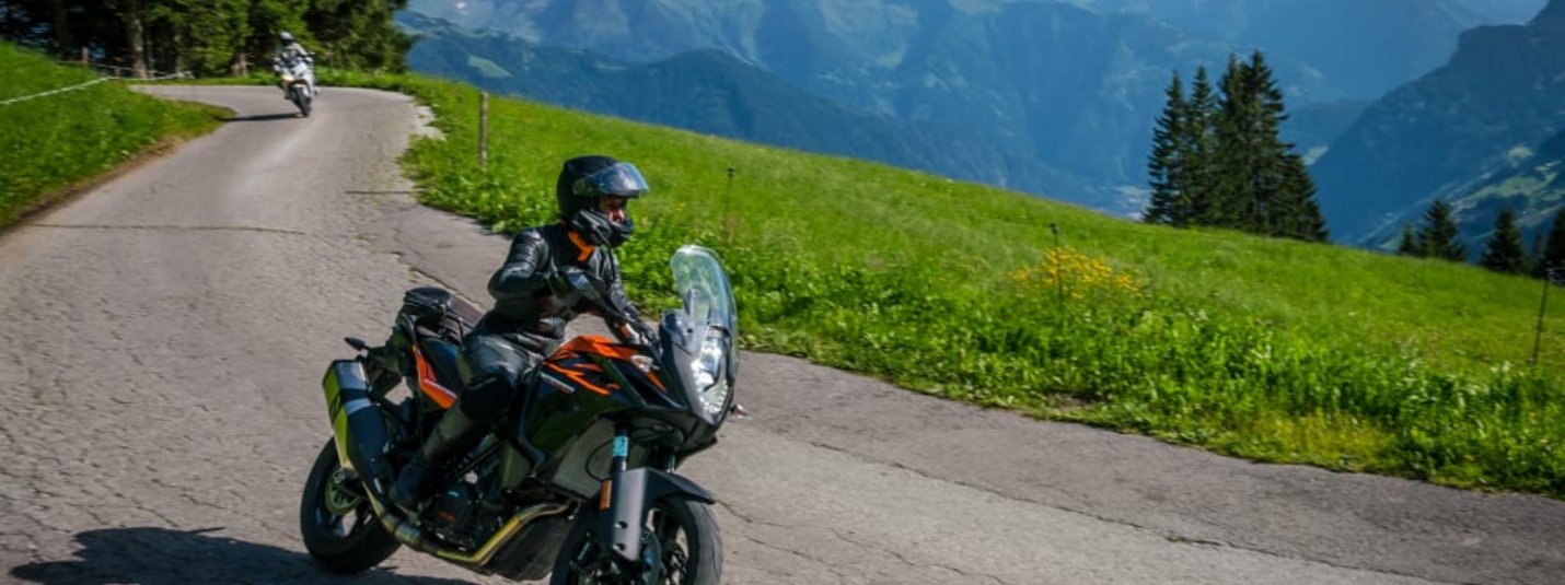 Motorradfahrer auf Bergstraße mit Alpen im Hintergrund