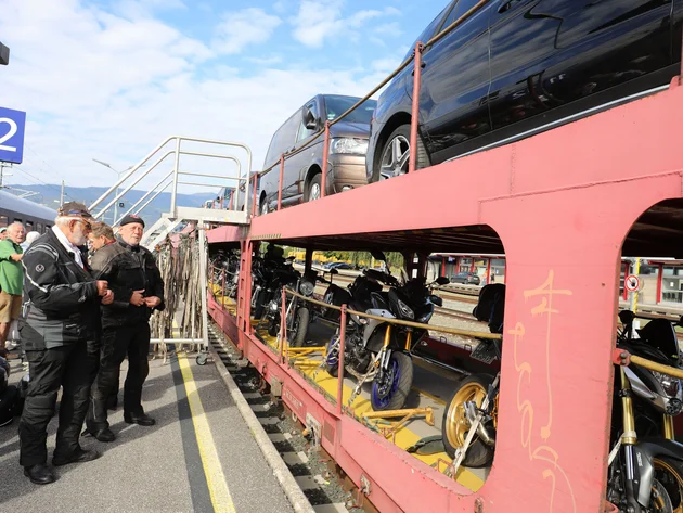 Personen am Bahnsteig neben Zug mit transportierten Motorrädern und Autos