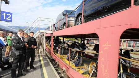 Personen am Bahnsteig neben Zug mit transportierten Motorrädern und Autos