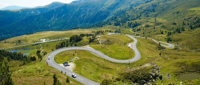 Niedere Tauern – Nockalm © Land Kärnten - Großglockner Hochalpenstraßen AG Serpentinenstraße in grüner Berglandschaft bei klarem Himmel