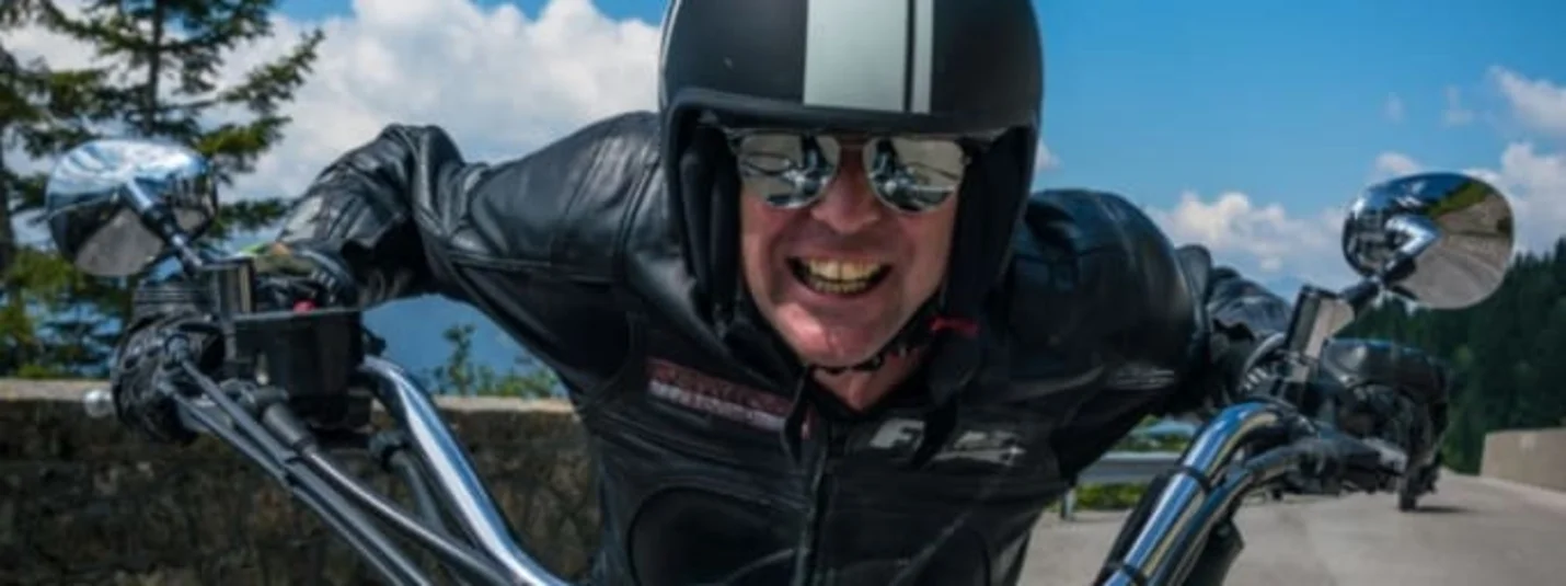 Stornofrei Lachende motorrijder in leren jas en helm onder blauwe lucht met Bikerweeks tekst