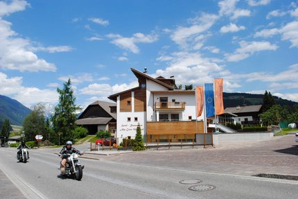 Motorradfahrer fahren an einem Hotel in den Bergen bei sonnigem Wetter vorbei