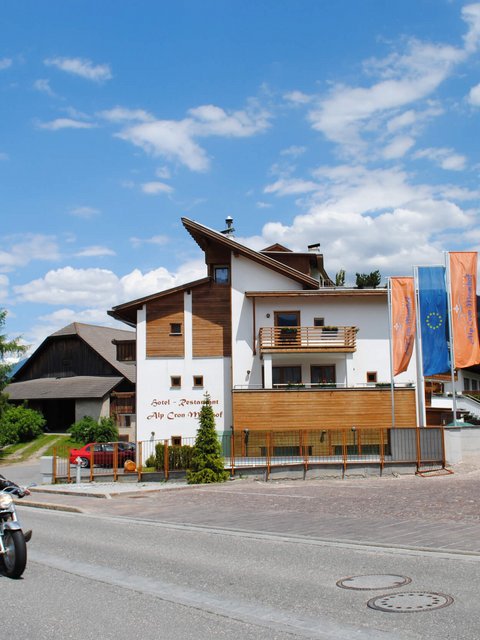 Motorradfahrer fahren an einem Hotel in den Bergen bei sonnigem Wetter vorbei