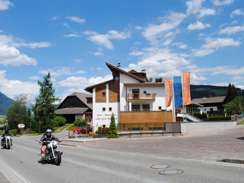 Motorradfahrer fahren an einem Hotel in den Bergen bei sonnigem Wetter vorbei