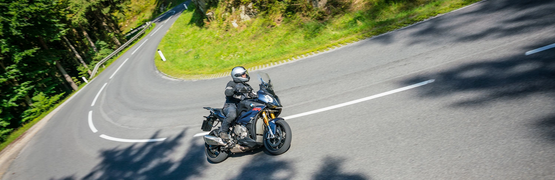 Motorcyclist speeding on winding mountain road with rocky cliff and forest