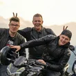 Drei Männer posieren mit Motorrädern vor einer Bergkulisse