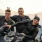 Three men pose with motorcycles against a mountain backdrop