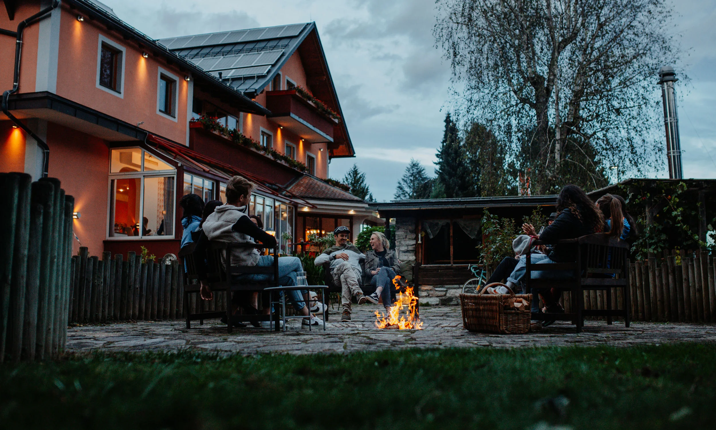 Gruppe von Menschen sitzt abends um ein Lagerfeuer im Garten eines Hauses