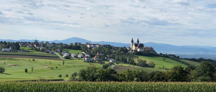 Blick auf Dorf und Kirche auf grünem Hügel unter bewölktem Himmel