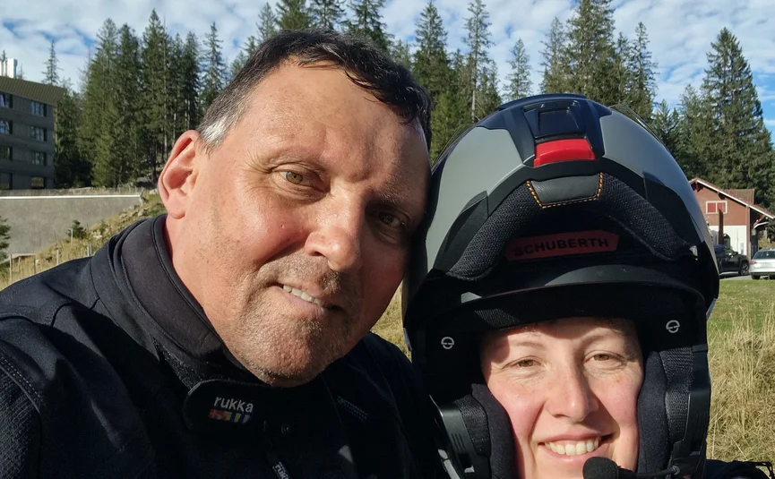 Two motorcyclists in gear posing in front of forest and blue sky