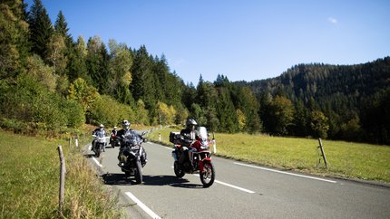 Motorradfahrer fahren auf Landstraße durch grüne Landschaft bei klarem Himmel