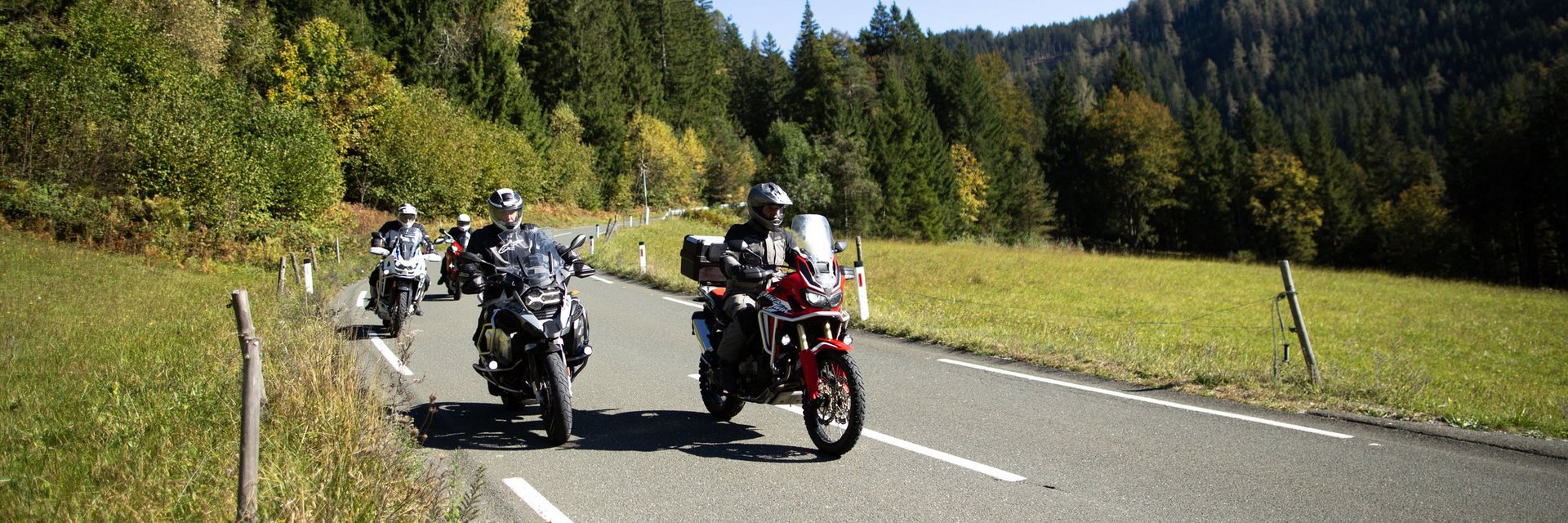 Motorradfahrer fahren auf Landstraße durch grüne Landschaft bei klarem Himmel