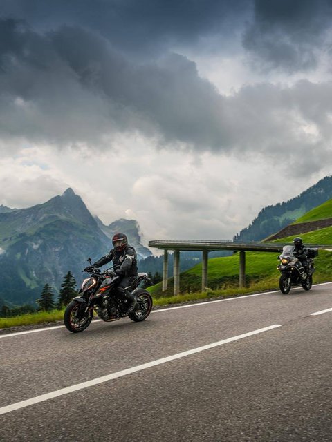 Zwei Motorräder auf bergiger Straße unter bewölktem Himmel