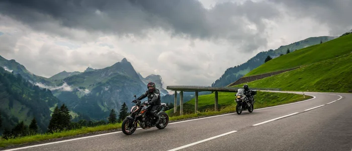 Two motorcycles on a mountain road under cloudy sky