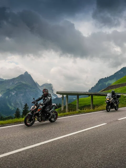 Two motorcycles on a mountain road under cloudy sky
