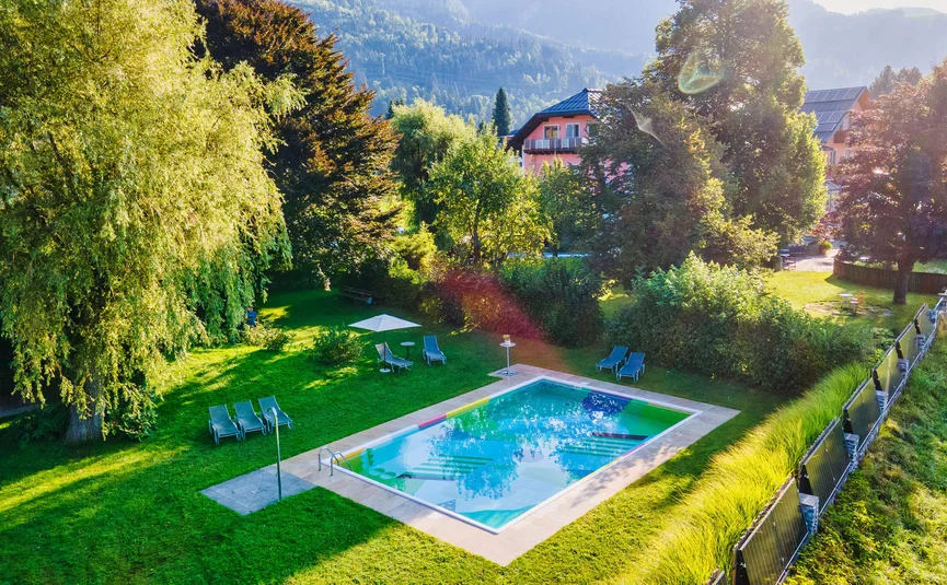 Garden swimming pool with sun loungers and green lawn surrounded by trees