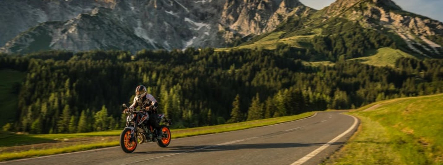 Motorradfahrer auf Bergstraße vor bewaldeten Bergen und blauem Himmel