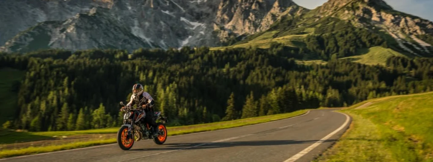6 days "toll included" Motorcyclist riding on mountain road with forest and rocky peaks