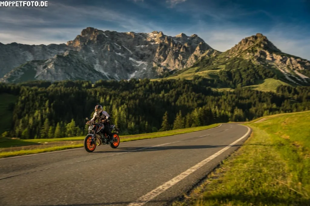 Motorcyclist riding on mountain road with forest and rocky peaks