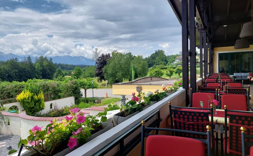 Balkon met rode stoelen en bloemen met uitzicht op groen landschap en bergen