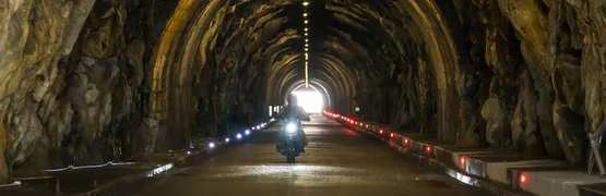 Motorradfahrer fährt durch beleuchteten Felsentunnel