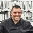 Smiling chef in black uniform in professional kitchen
