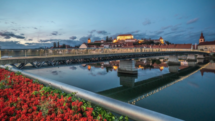 Verlichte brug en kasteel met stad aan rivieroevers bij schemering