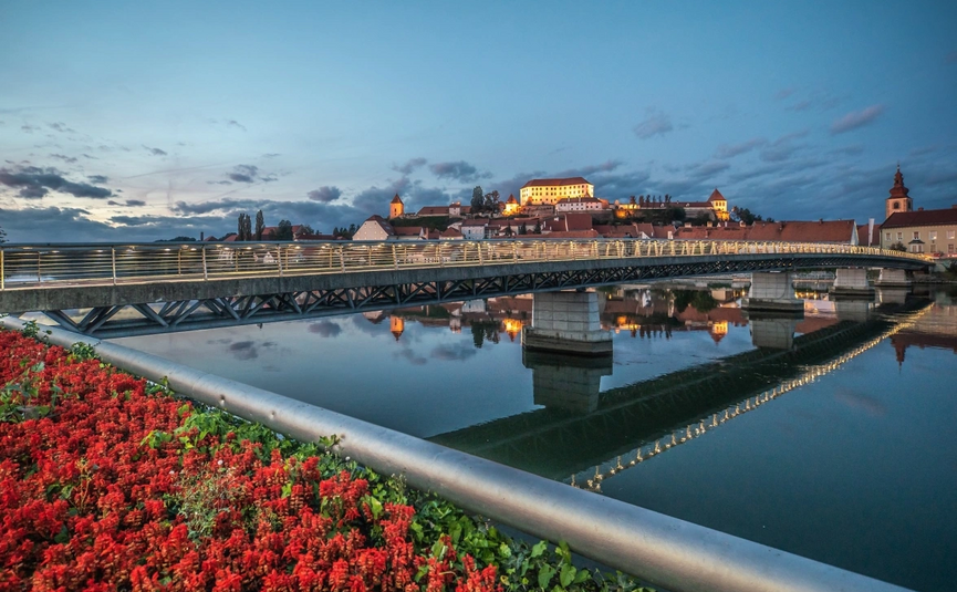 Verlichte brug en kasteel met stad aan rivieroevers bij schemering