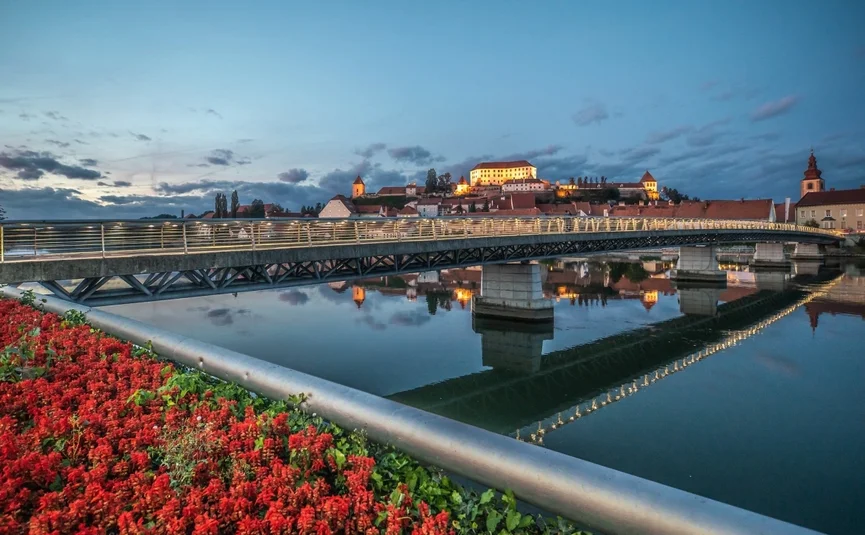 Wijnroute Karinthië-Styrië Verlichte brug en kasteel met stad aan rivieroevers bij schemering