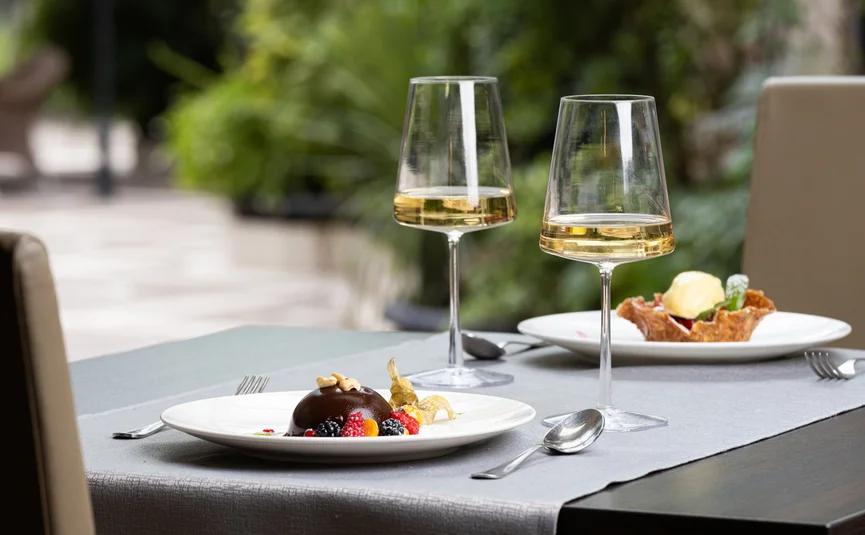 Zwei Gläser Weißwein und Desserts auf gedecktem Tisch im Restaurant