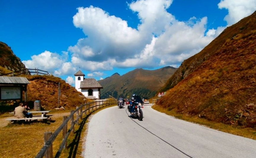 Motorradfahrer fahren auf Bergstraße neben Kapelle bei sonnigem Himmel