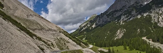 Bergweg met groen en beboste bergen onder bewolkte lucht