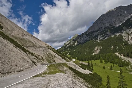 Mountain road winding through green and forested mountains under cloudy sky