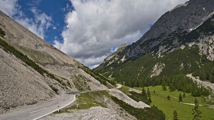 Gebirgsstraße mit Grünflächen und bewaldeten Bergen unter bewölktem Himmel