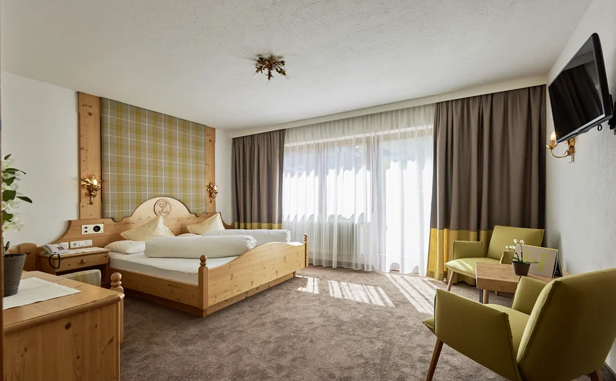 Bright hotel room with wooden bed, two chairs, and wall-mounted TV