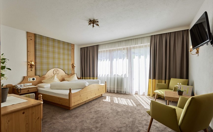 Helles Hotelzimmer mit Holzbetten, zwei Stühlen und TV an der Wand