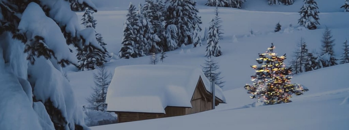 Schneebedeckte Hütte und beleuchteter Tannenbaum in verschneiter Winterlandschaft