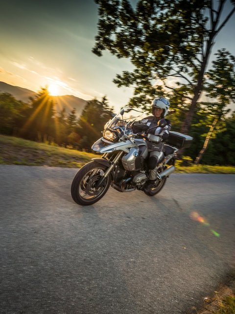 Motorradfahrer auf kurviger Straße bei Sonnenuntergang in ländlicher Umgebung